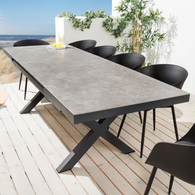 An outdoor dining table and chairs set on a wooden deck with a beach and ocean in the background.