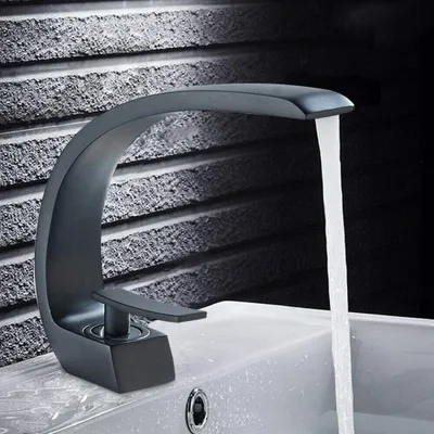 A black modern faucet is shown in use, with water flowing into a white sink. The background is a textured gray wall.