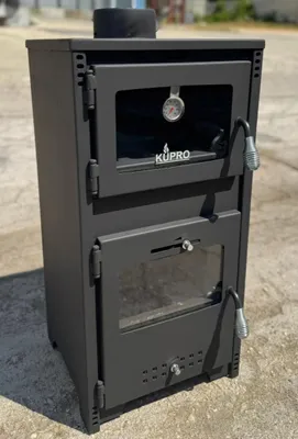 A black wood-burning stove with a glass door and a thermometer is shown outdoors on a paved surface.