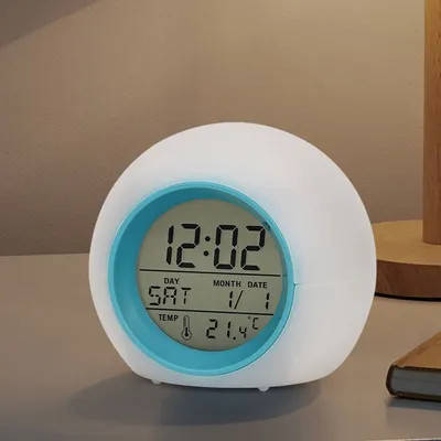 A digital alarm clock with a light-up feature sits on a table.