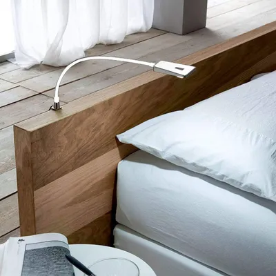 A bedside lamp attached to a wooden headboard, next to a bed with white linens.