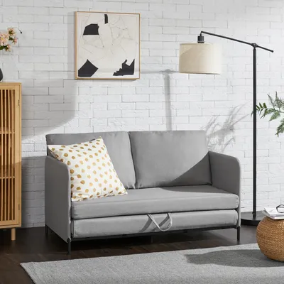 A gray sofa with a patterned pillow is shown in a room with a brick wall and a floor lamp.