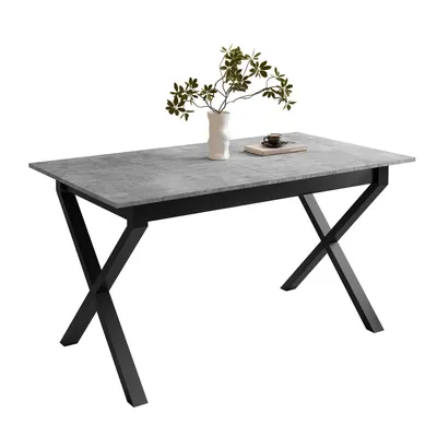 A dining table with a grey textured top and black X-shaped legs, decorated with a vase of plants and a book with a cup on it.