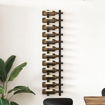 A black metal wine rack mounted on a white wall, holding 12 bottles of wine. A large green plant is visible on the left side of the image.
