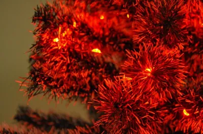 A close-up view of red Christmas tree tinsel with small orange lights.