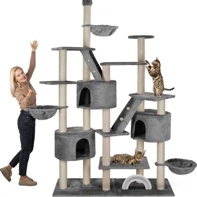 A woman is posing next to a large, multi-level cat tree. Two cats are also present on the cat tree.