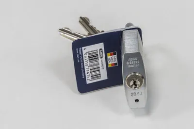 A silver padlock with two keys attached to a blue tag, lying on a white surface.