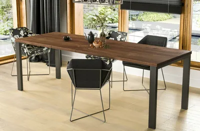 A dining table with chairs in a well-lit room with large windows overlooking a garden.