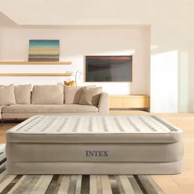 An inflatable mattress is placed in a living room setting, with a sofa and TV in the background.