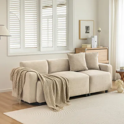 A beige sofa with a throw blanket and pillows in a living room setting.