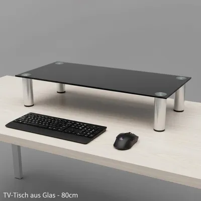 A glass monitor stand is shown on a desk with a keyboard and mouse.