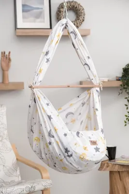 A baby hammock with a moon and star pattern hanging in a room, next to a chair and a table.