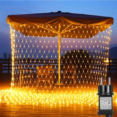 A patio umbrella decorated with yellow net lights at dusk, with chairs and tables visible underneath.