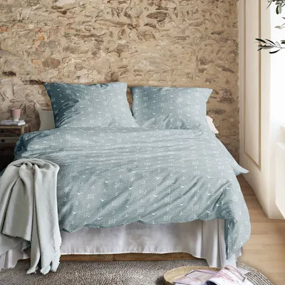 Hellblau-grüne Bettwäsche mit weißen nautischen Motiven auf Doppelbett vor rustikaler Steinwand in gemütlichem Schlafzimmer