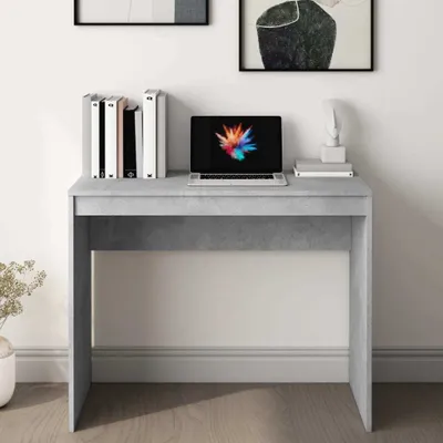 A modern desk with a laptop and books on top, set against a white wall with artwork.