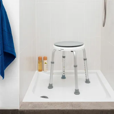 A shower stool in a shower stall with two bottles of toiletries and a blue towel.