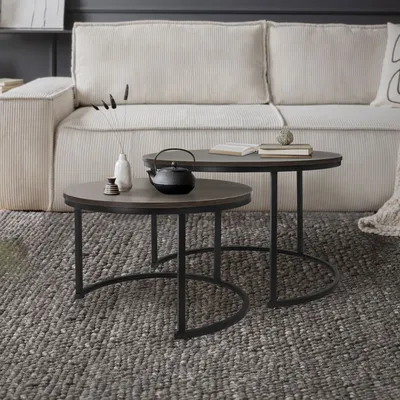 Two nesting coffee tables are placed on a textured rug in front of a sofa.