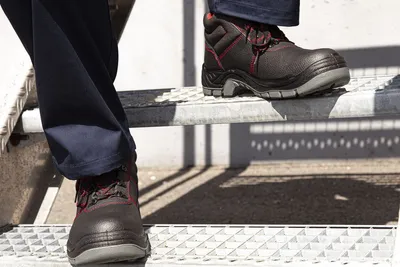 A person wearing work pants and safety shoes is walking up a set of metal stairs.
