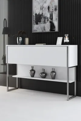 A white console table with silver legs, decorated with three dark vases on the lower shelf, against a black slatted wall.