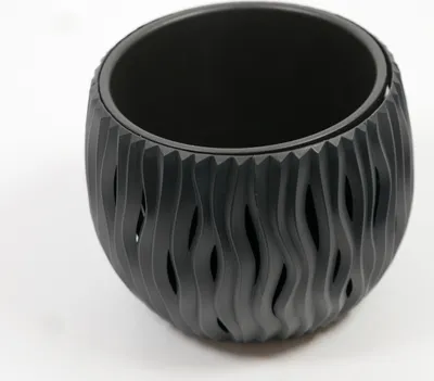 A black planter with a wavy, cut-out design sits on a white surface.
