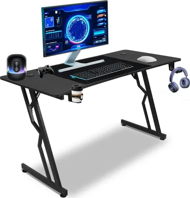 A gaming desk setup with a monitor, keyboard, mouse, controller, headphones, and a cup holder.