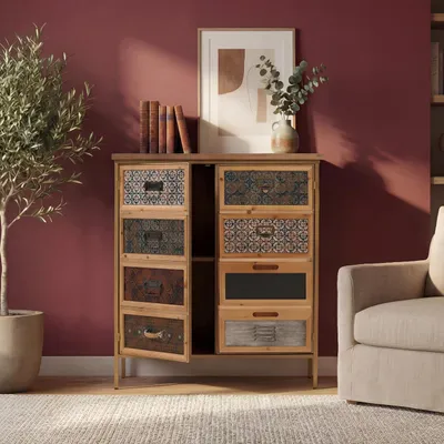 A vintage-style apothecary cabinet with multiple drawers, placed in a room with a red wall and a beige armchair.