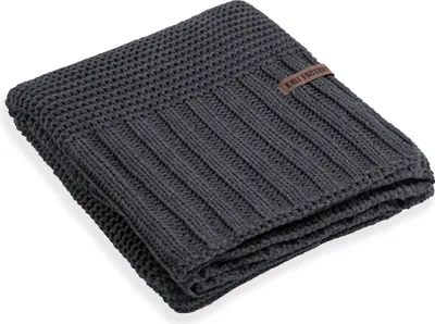 A folded gray knitted blanket with a brown leather tag.