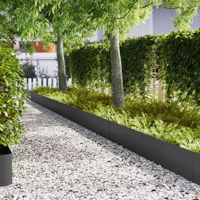 A garden path with white gravel, bordered by a black metal edging and lush green plants and trees.