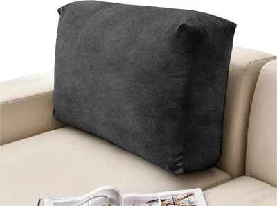 A dark gray cushion is placed on a beige sofa. A magazine is open on the sofa in front of the cushion.