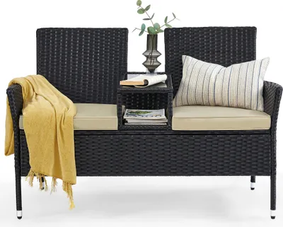 A black rattan bench with beige cushions and a yellow throw blanket.