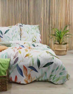 A bed with a floral duvet cover and pillows, set against a bamboo wall, with a potted plant to the side.
