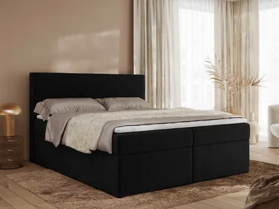 A bedroom scene with a black boxspring bed as the main focus, styled with bedding and a bedside table with a lamp.