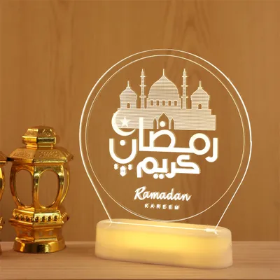 A Ramadan-themed LED lamp and two decorative lanterns are displayed on a wooden surface against a wooden background.