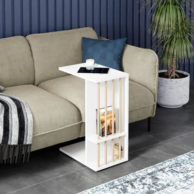 A white side table with books and a cup of coffee is placed next to a beige sofa in a living room setting.