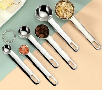 A set of stainless steel measuring spoons arranged diagonally on a light green and peach background.