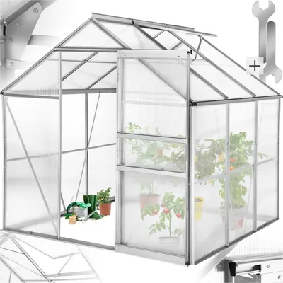 A greenhouse with plants inside, showing gardening tools near the entrance.