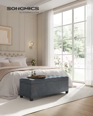 A bedroom scene with a bed, window, and a storage ottoman in the foreground.