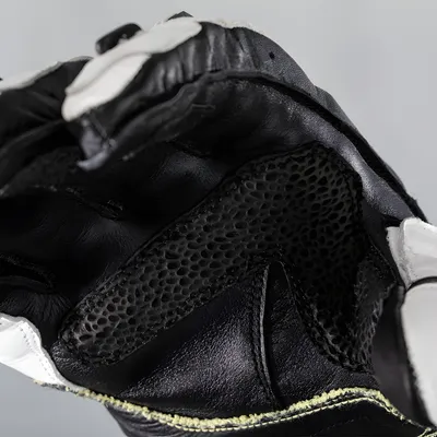 A close-up view of a black and white motorcycle glove, focusing on the textured material and stitching.