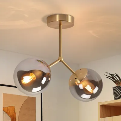 A close-up shot of a modern, two-light ceiling lamp with gold metal accents and clear glass globes.