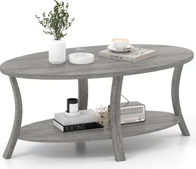 A gray oval coffee table with two shelves, decorated with a plant, books, a cup of coffee, and a vintage radio.