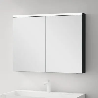 A mirrored cabinet with two doors is mounted on a wall above a sink with a faucet.