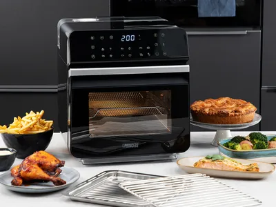 A Princess air fryer oven is shown on a kitchen counter, surrounded by various cooked foods.