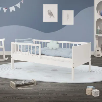 A child's bedroom with a white toddler bed, bedding, and decorative elements.