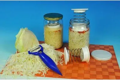 A setup for making sauerkraut or pickles, with jars, cabbage, and a peeler.