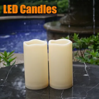 Two LED candles are placed on a marble table in front of a fountain and pool.