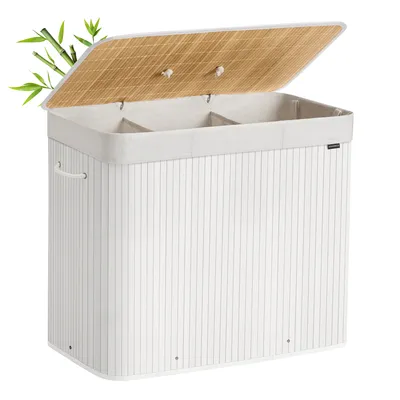 A white laundry basket with a bamboo lid and three compartments, shown with a few bamboo leaves on the side.