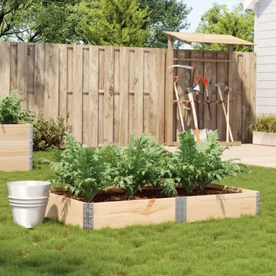 A raised garden bed with plants, a wooden fence, and gardening tools in a backyard setting.