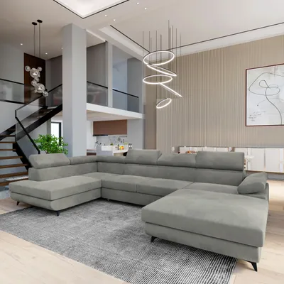 A spacious, modern living room with a large U-shaped sectional sofa as the focal point. The room features a high ceiling, a staircase, and contemporary decor.