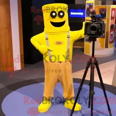 Immagine prodotto di Personaggio in costume mascotte REDBROKOLY fotocamera gialla vestito con jeans bootcut e fermacravatta