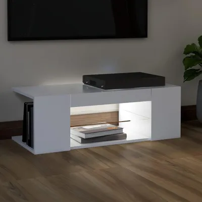 A white TV stand with a black electronic device on top and books inside.